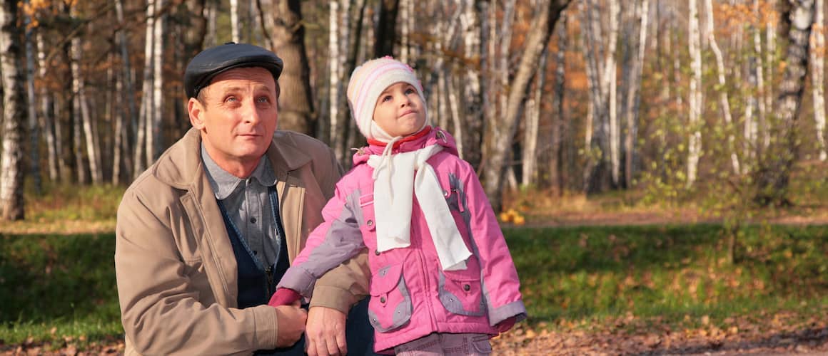 Grandfather with granddaughter in park in autumn look upward