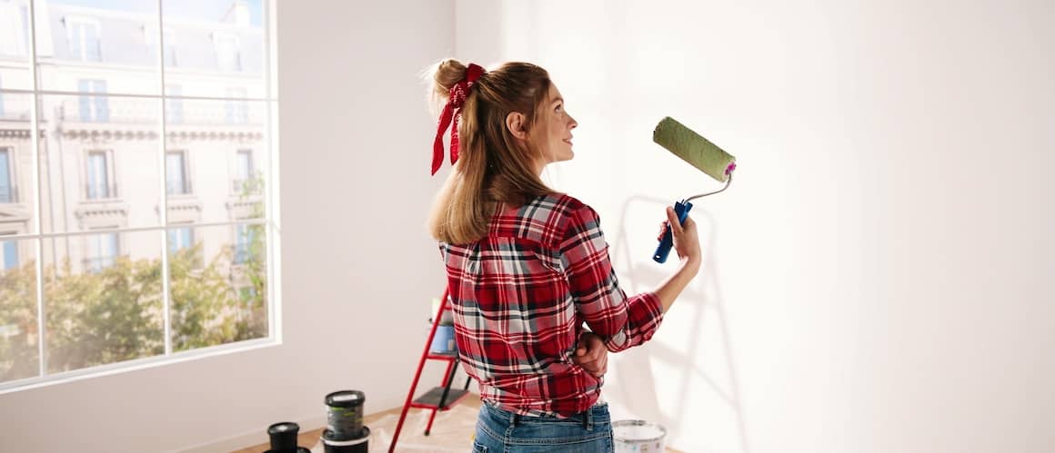 A woman painting a home in green, illustrating a woman painting the exterior of a house in green color.