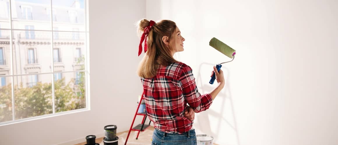 A woman painting a home in green, illustrating a woman painting the exterior of a house in green color.