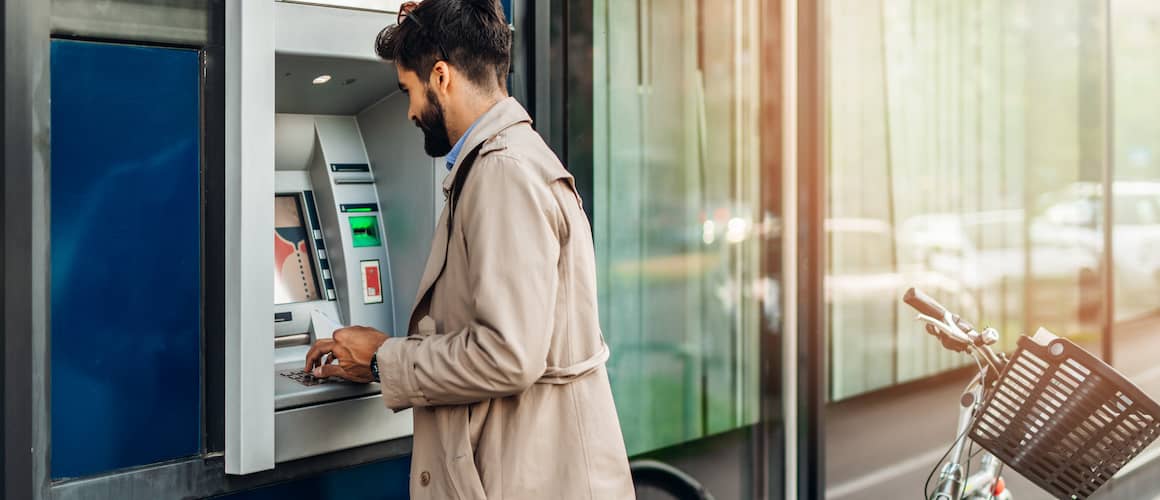 Young bearded man using atm machine to withdraw money