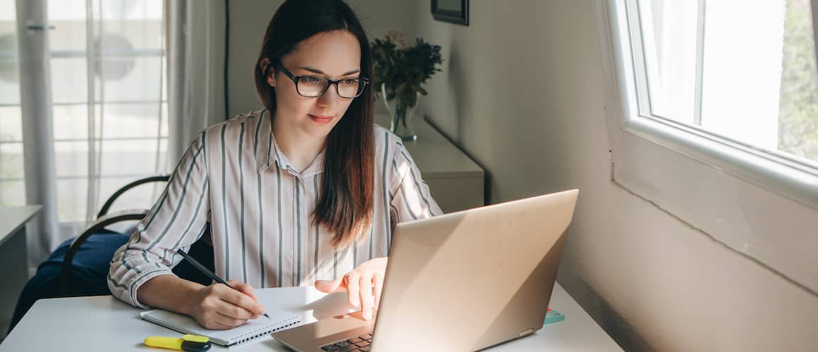 A woman researching and writing on a notepad, potentially related to real estate planning or financial research.