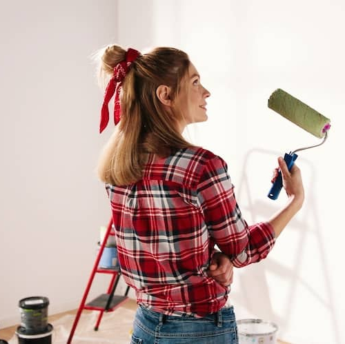 A woman painting a home in green, illustrating a woman painting the exterior of a house in green color.