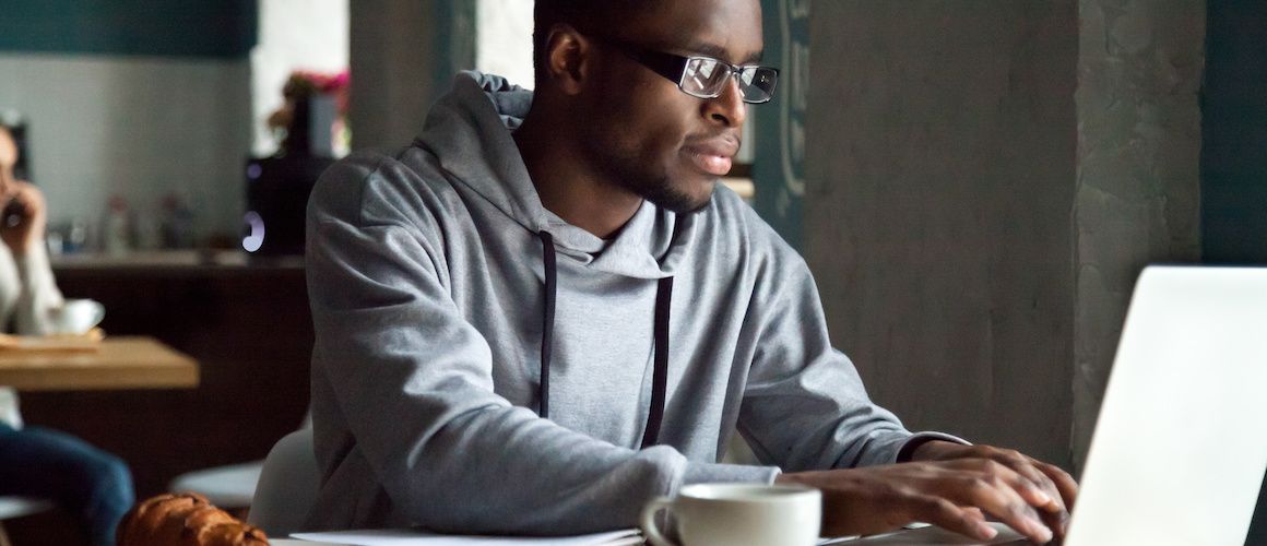 Young African American man in a hoodie using a laptop.