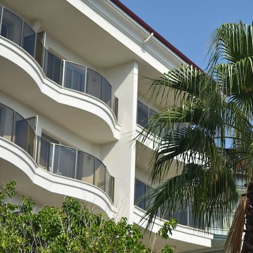 White historical condo building with balconies and palm trees out front.
