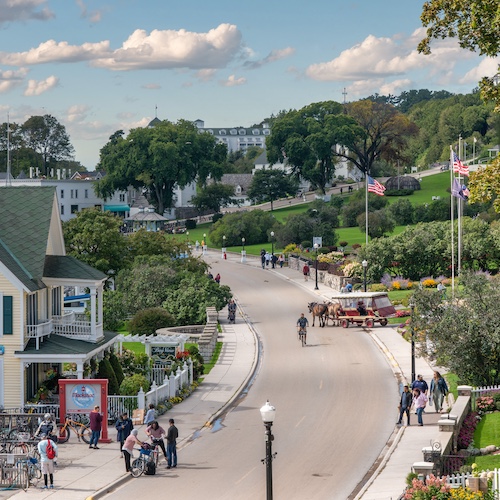 Main street on Mackinac Island in Michigan, dotted with pedestrians and horse carriages.