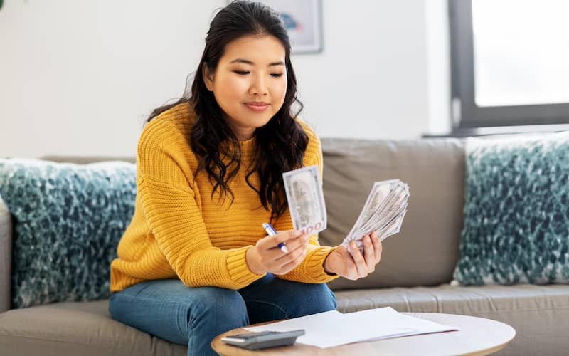 Woman in yellow sweater sitting on the couch counting dollars.