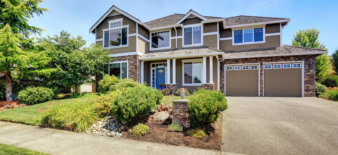 Big, multi-story American home with a lot of greenery out front.