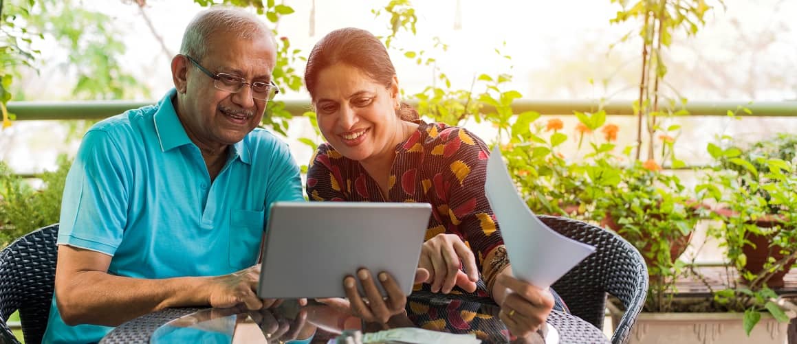 Close-up of older couple in glasses reviewing financial documents at dining table.