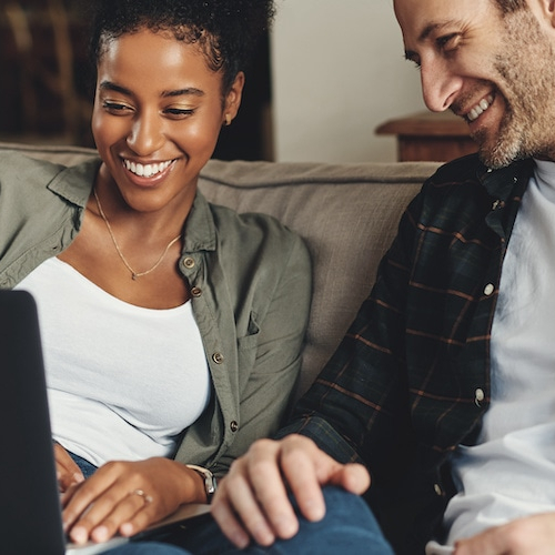 A smiling couple seated comfortably on a couch, expressing contentment.