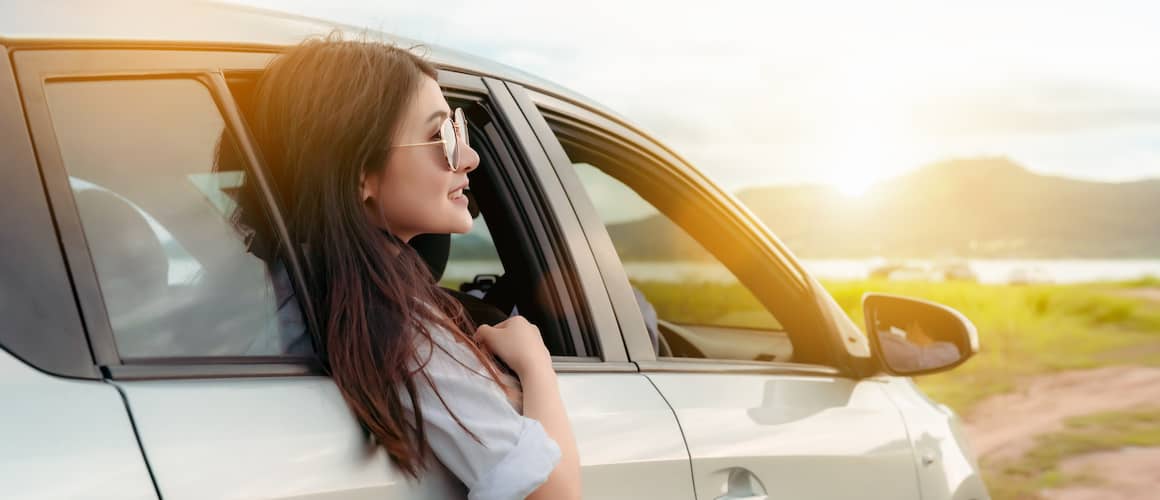 Woman wearing sunglasses riding in backseat of SUV on a roadtrip at sunrise.