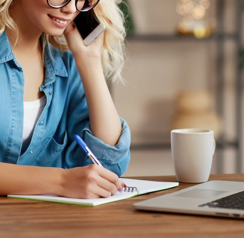 A blonde woman writing notes while on the phone, potentially related to real estate or work-related tasks.