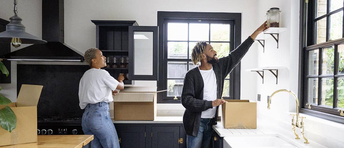 A young black couple moving into a new home, carrying boxes and belongings.