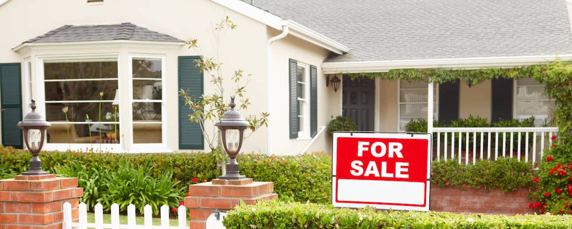 Yellow house for sale with brick walkway, hedges and red flowering bushes