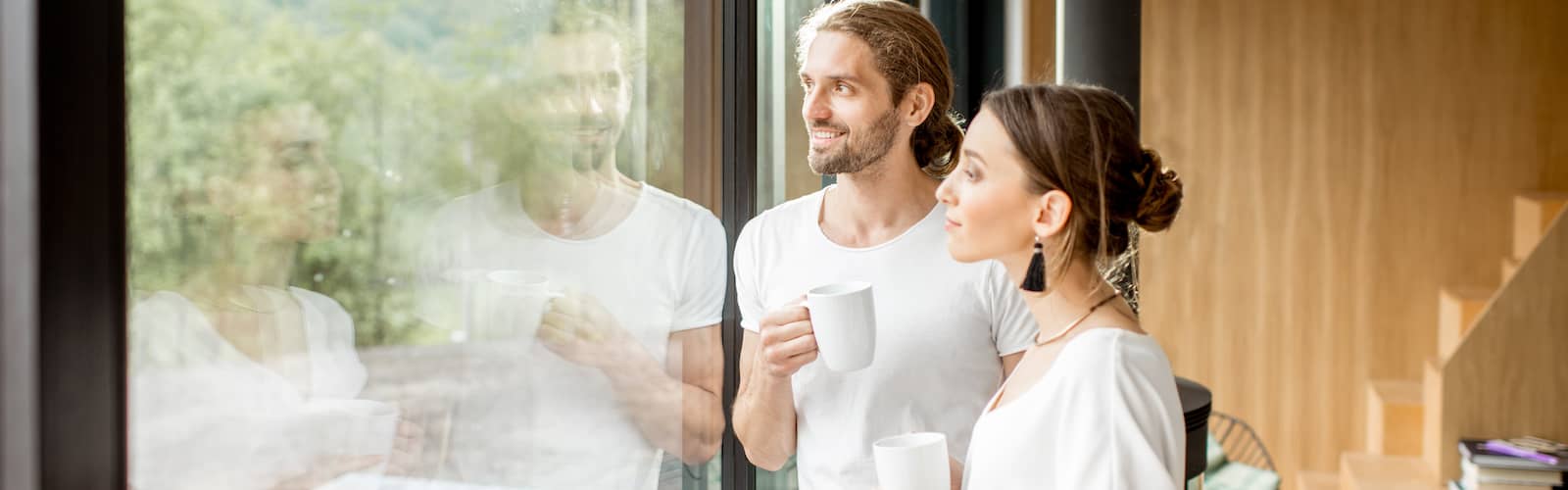 A couple holding cups looking outside the glass window.