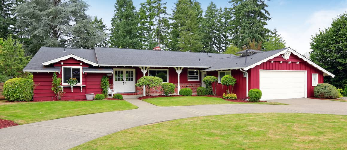 A red one-story home with a neatly trimmed lawn and trees, presenting a cozy residential scene.