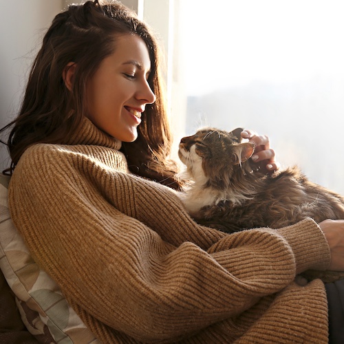 Young woman smiling while cuddling her pet cat at home.
