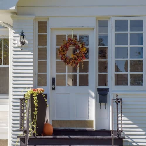 Front view of white bungalow with autumn wreath and pumpkin on top step.