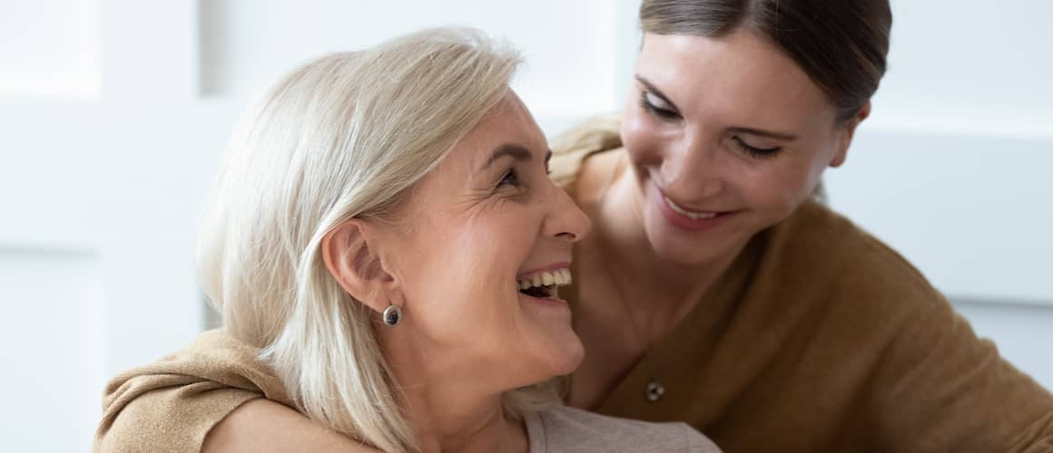 Woman hugs her senior mother as both laugh.