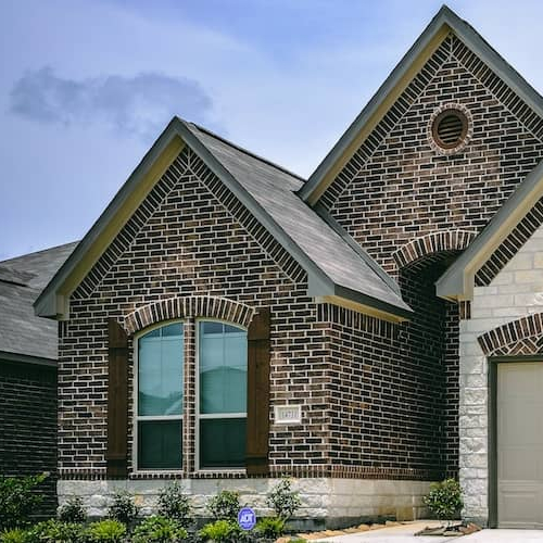 A dark brown and light brown speckled brick home with a white sandstone garage, showcasing unique exterior materials.