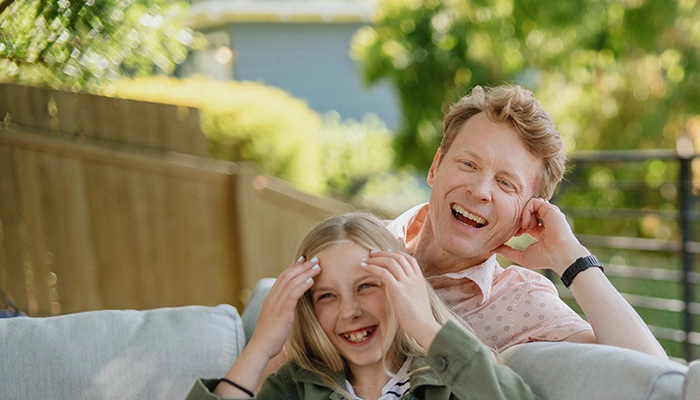 Mom and father laughing on outdoor couch with mom partially out of frame.