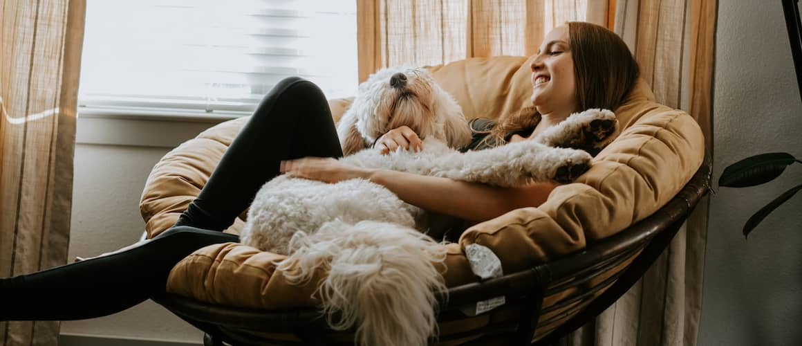 Young lady sitting in a moon shaped chair with a dog in her lap.