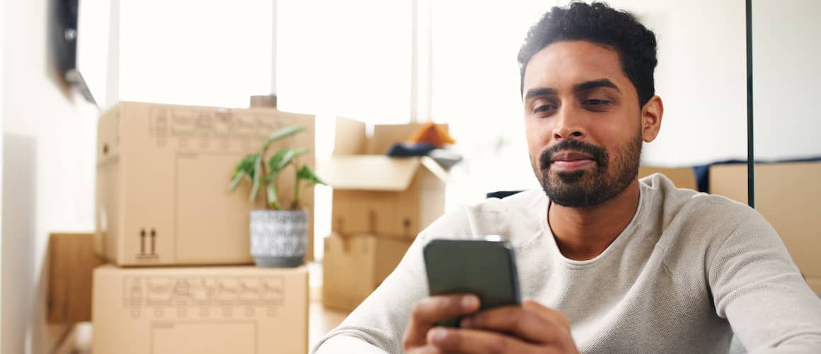 A person looking at his phone surrounded by boxes indicating he just moved into a new house or apartment.