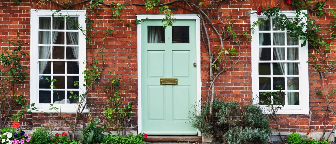 A red brick home front with teal colored door and plant vines.