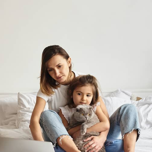 A women with her daughter holding a cat looking at some information on the laptop.