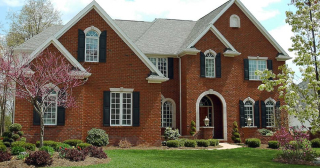 A stately red brick home with black shutters and white trim surrounded by a landscaped yard.
